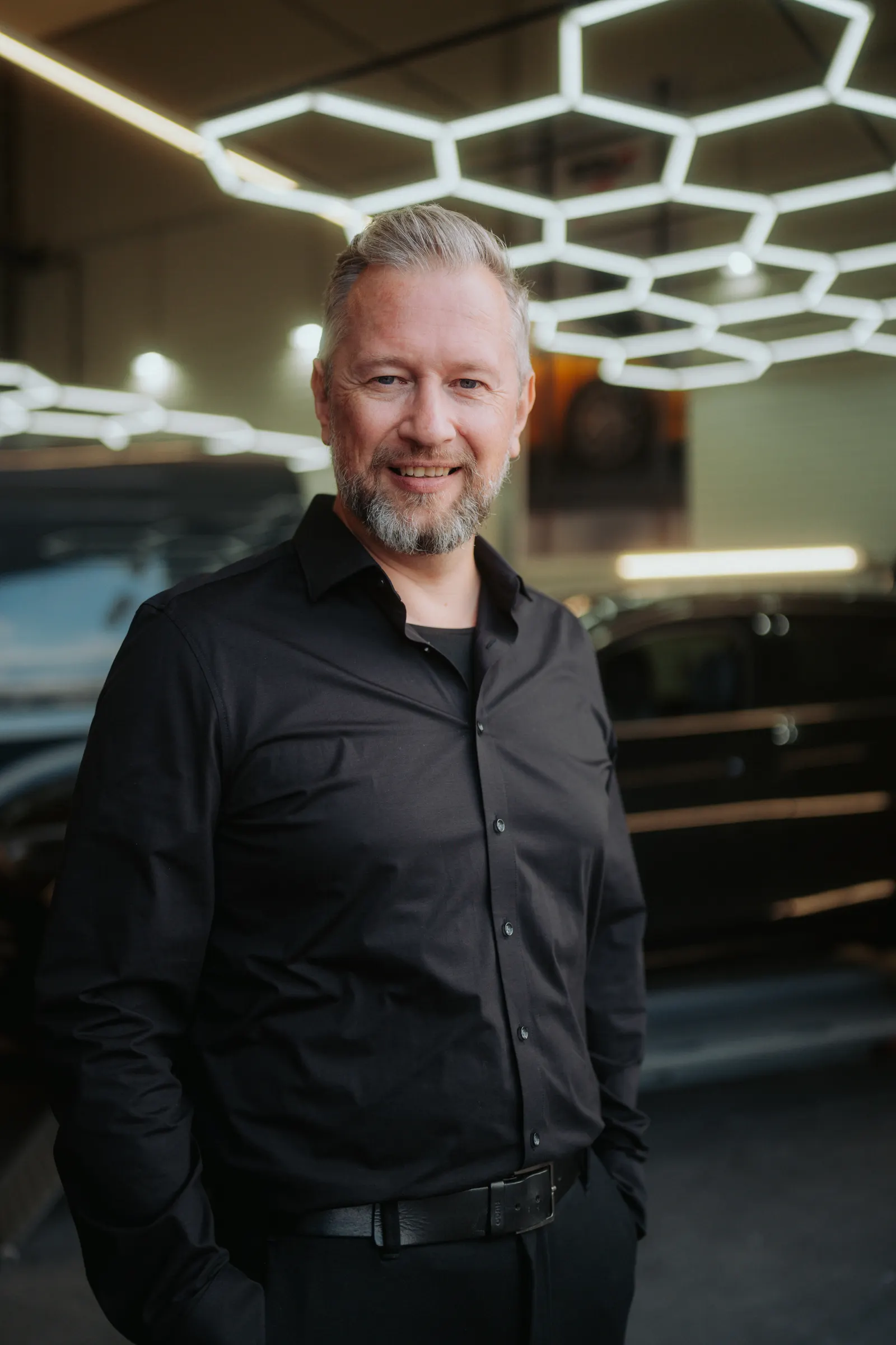Tim Klötzing in schwarzem Hemd vor einem Fahrzeug in der Werkstatt eines Autohauses