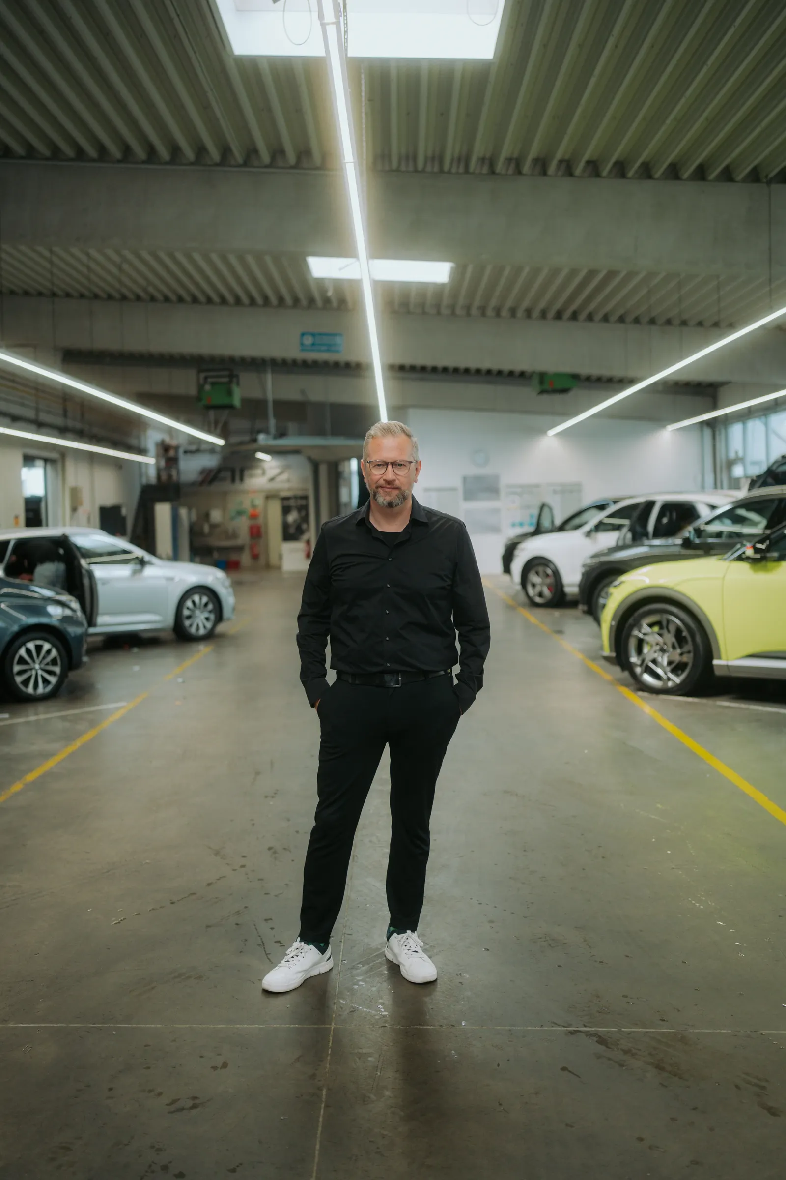 Tim Klötzing in schwarzem Hemd, die Hände in den Taschen, in der Halle eines Autohauses zwischen Fahrzeugen