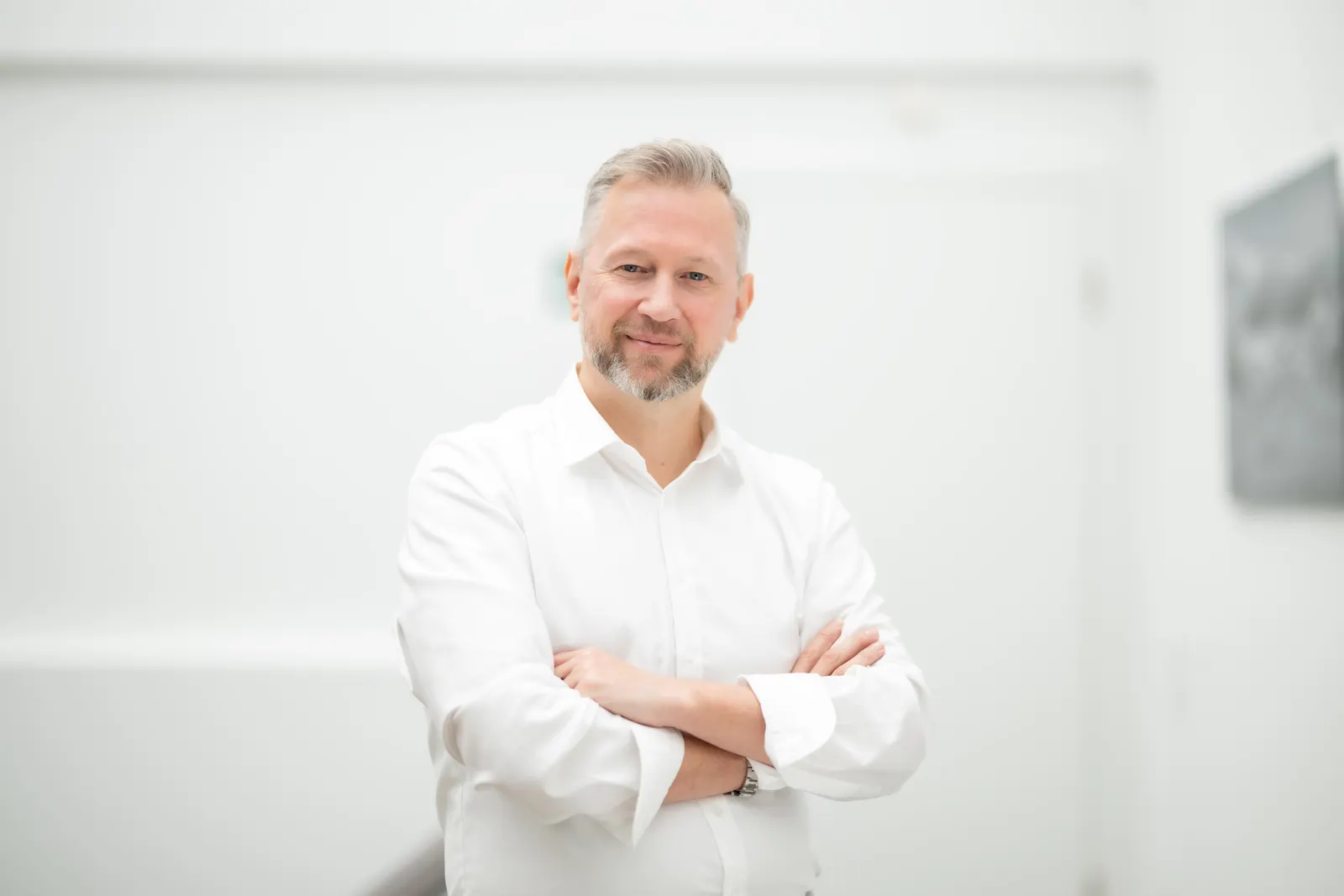 Tim Klötzing in weißem Hemd mit verschränkten Armen vor heller Wand