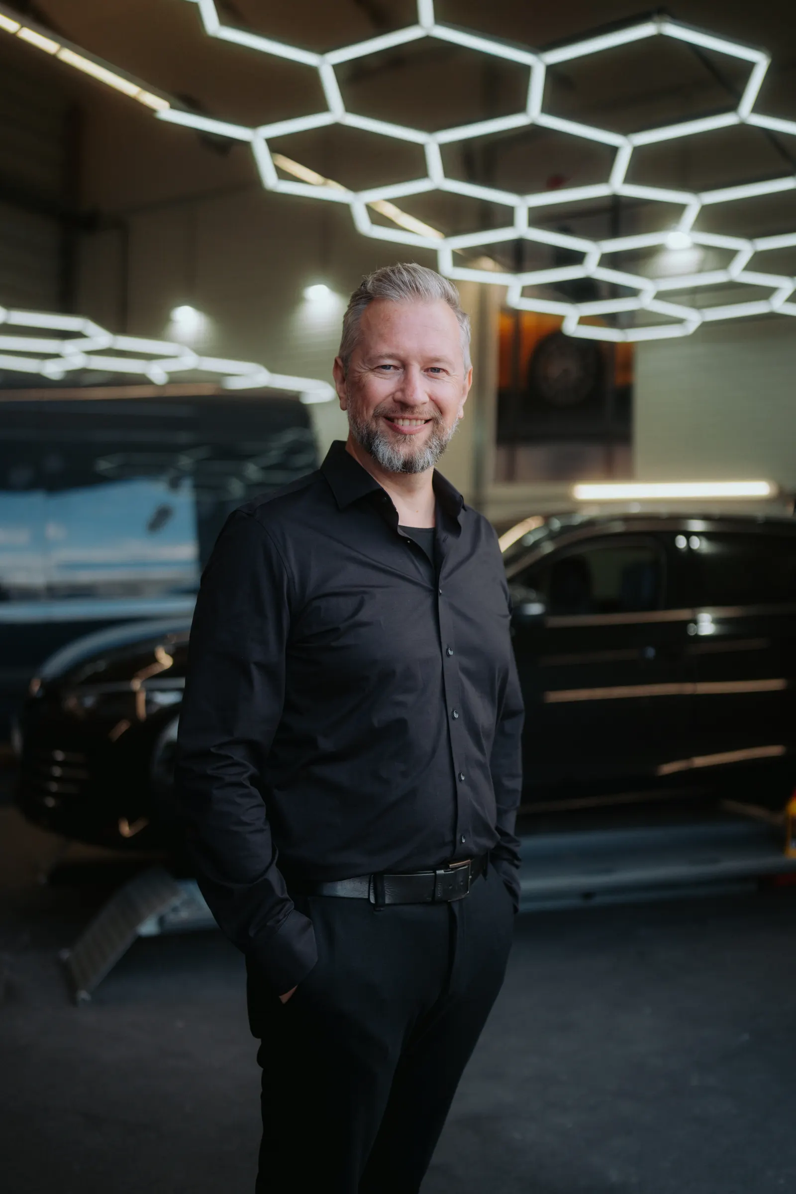 Tim Klötzing in schwarzem Hemd in einer Autohaus-Werkstatt unter Wabenleuchten